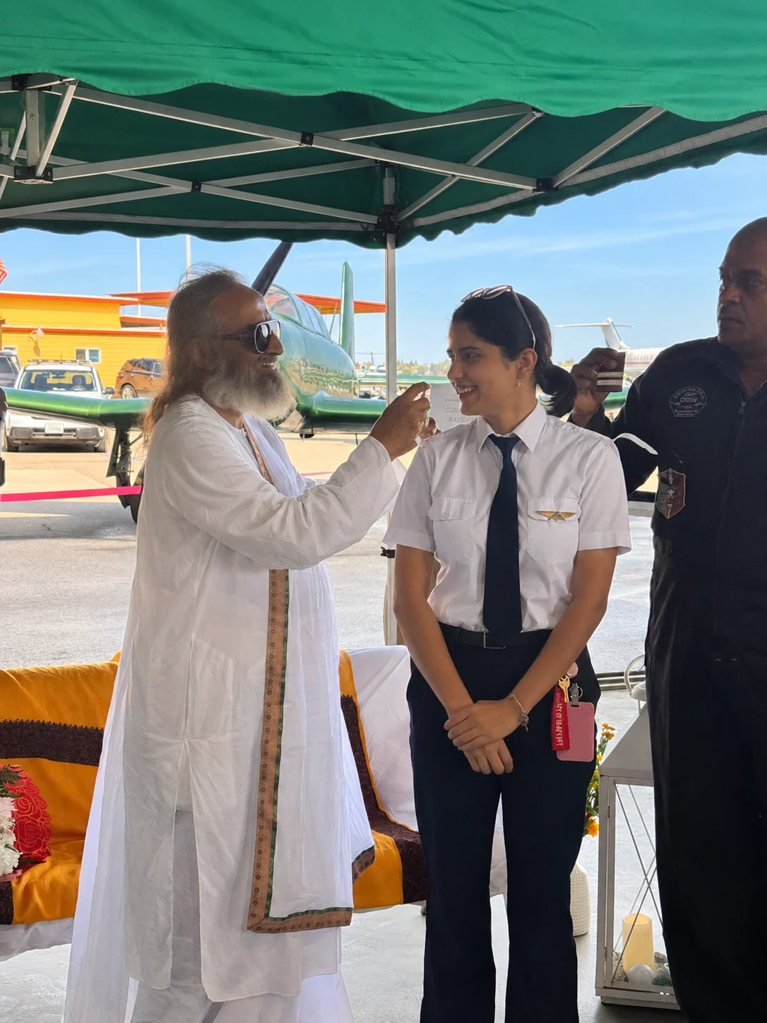 A cadet in uniform receiving a tilak at a ceremony beside the flight line, training aircraft behind