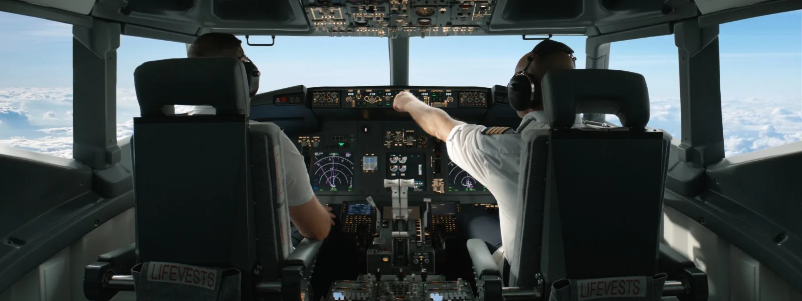 Two pilots at the controls of an airliner cruising above the clouds
